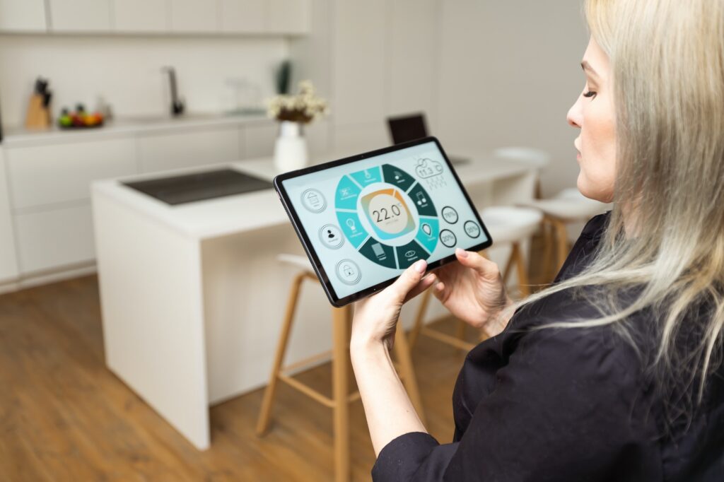 Woman pushing button on kitchen app of smart home on digital tablet at home. Concept of modern home